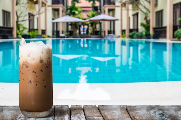 Un vaso de café helado en la mesa de madera junto a la piscina