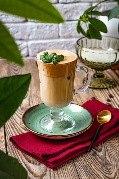 Un vaso de café con leche decorado con hojas de menta sobre la mesa de un café, café dalgona, foto vertical.