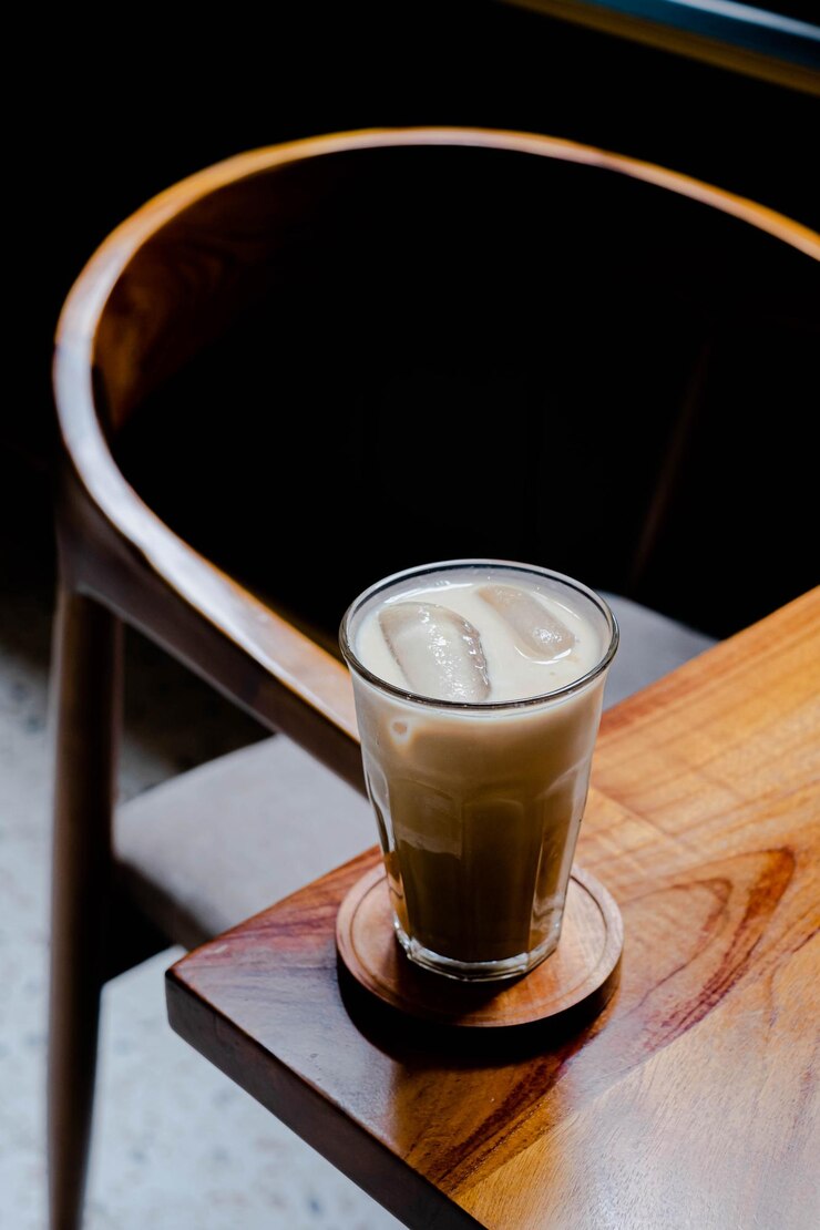 Un vaso de café con leche helado en un posavasos y una mesa de madera