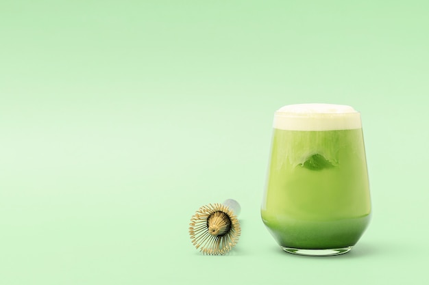 Un vaso de café con leche matcha helado sobre un fondo verde con espacio de copia.