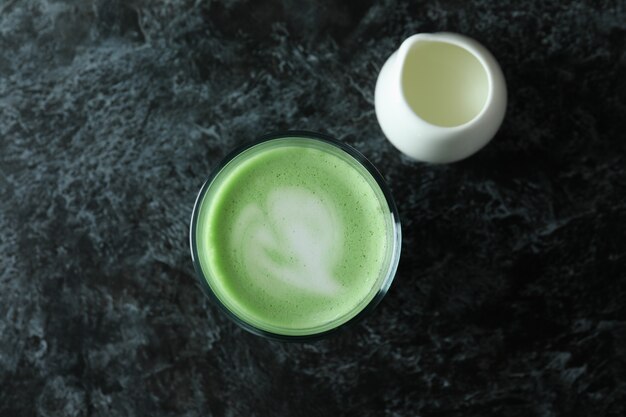 Vaso de café con leche matcha y leche sobre fondo negro ahumado