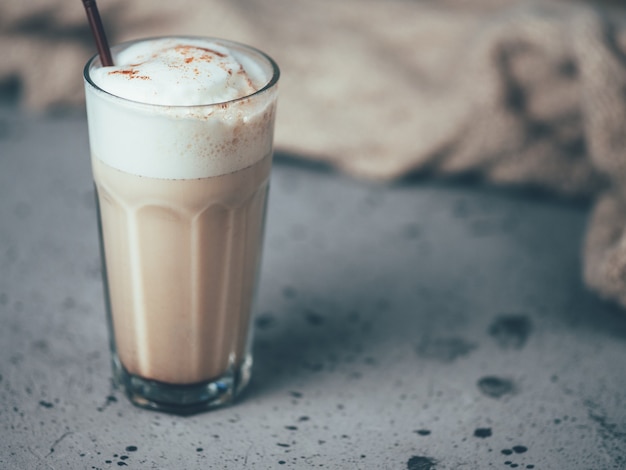 Un vaso de café con leche en una mesa gris con una bufanda de otoño. Estilo Hygge. Confort en el hogar