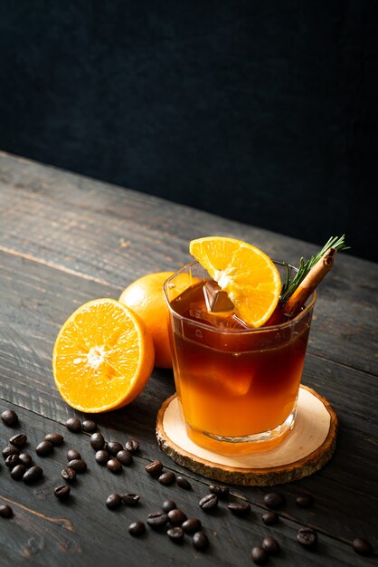 Foto un vaso de café negro americano helado y una capa de jugo de naranja y limón decorado con romero y canela.