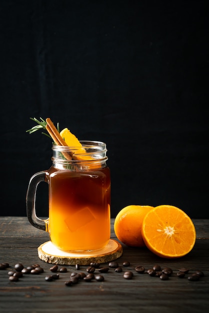 Un vaso de café negro americano helado y una capa de jugo de naranja y limón decorado con romero y canela.