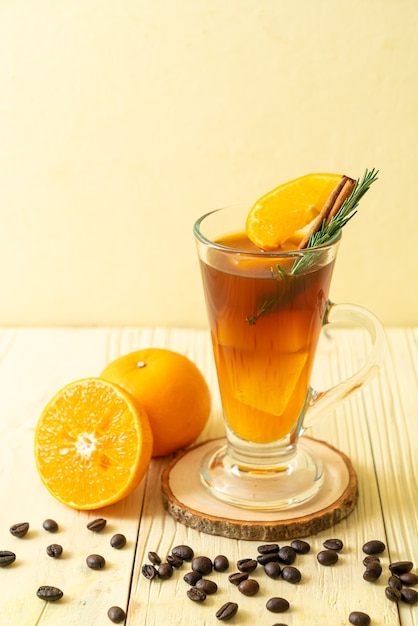 Un vaso de café negro americano helado y una capa de jugo de naranja y limón decorado con romero y canela.