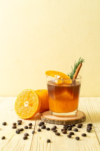 Un vaso de café negro americano helado y una capa de jugo de naranja y limón decorado con romero y canela.