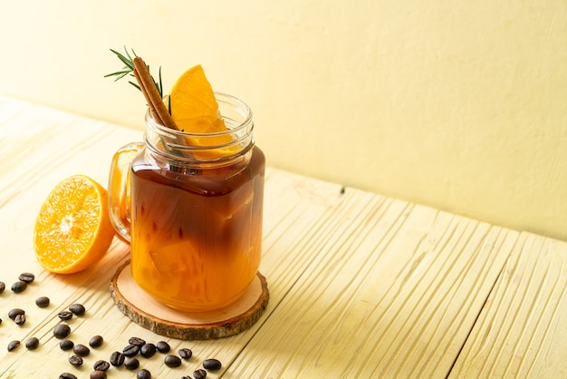 Un vaso de café negro americano helado y una capa de jugo de naranja y limón decorado con romero y canela.