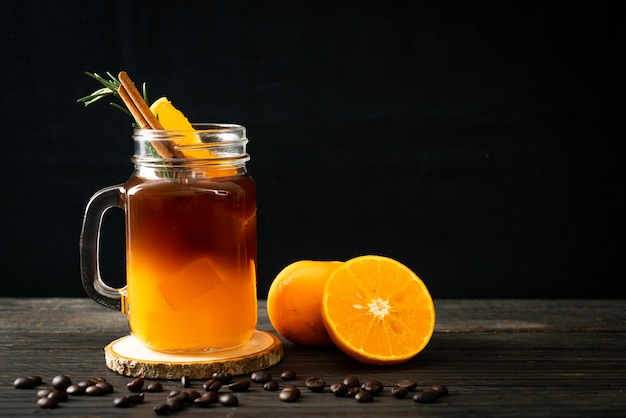 Un vaso de café negro americano helado y una capa de jugo de naranja y limón decorado con romero y canela.