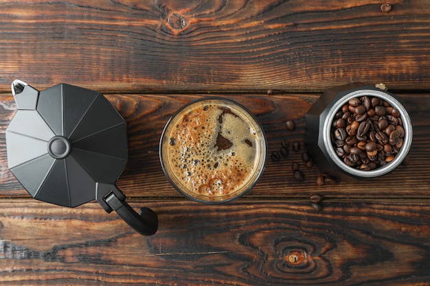 Vaso de café recién hecho, cafetera y granos de café en la mesa de madera