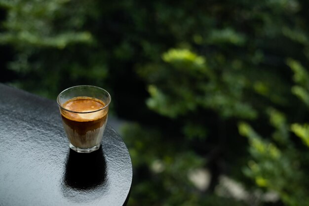 Un vaso de café se sienta en un balcón con un fondo verde.