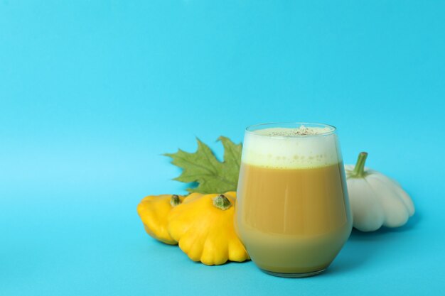 Vaso de calabaza con leche e ingredientes sobre fondo azul.