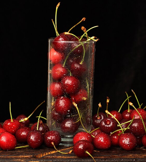 Vaso con cerezas maduras sobre un fondo oscuro con gotas de agua.