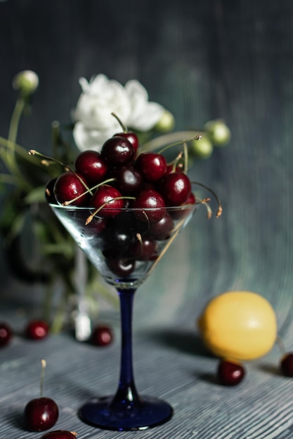 Un vaso de cerezas se sienta en una mesa con un limón en el fondo.