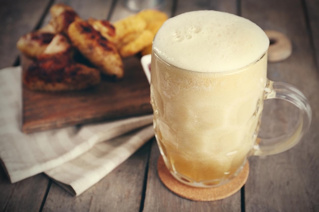 Vaso de cerveza y alitas de pollo en la mesa de madera de cerca