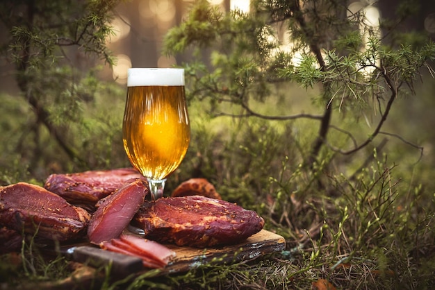 Vaso de cerveza artesanal helada con carne de cerdo ahumada en frío casera en una tabla de madera rústica poco profunda