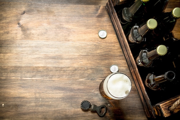 Vaso de cerveza con una caja y un abridor de botellas. Sobre una mesa de madera.