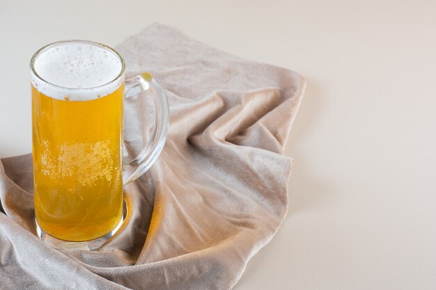 Vaso de cerveza dorada fría aislado sobre un mantel ligero