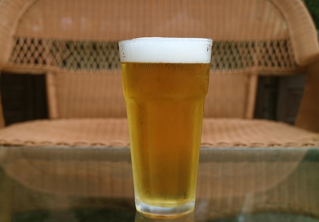 Un vaso de cerveza fría aislado en la mesa con silla vacía borrosa