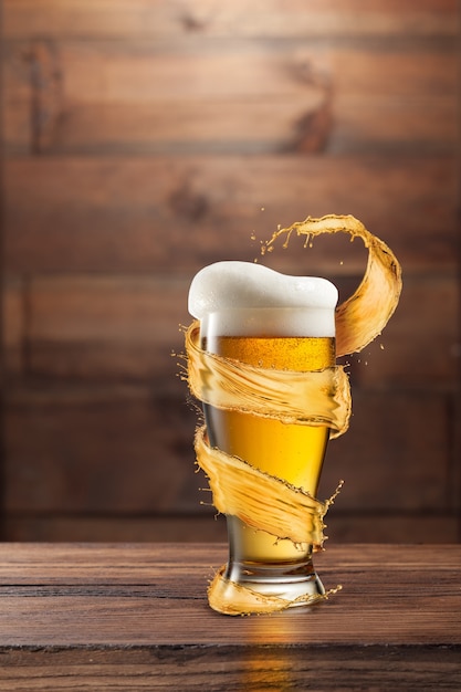 Un vaso de cerveza fría con gotas y espuma alrededor de un toque en una madera oscura con espacio de copia.