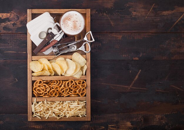 Vaso de cerveza lager artesanal en caja vintage de abridores de aperitivos y esteras de cerveza sobre fondo de madera Pretzel y patatas fritas y patata salada