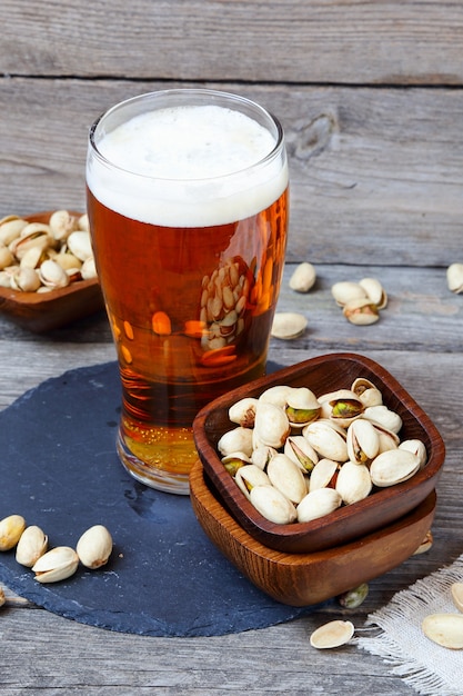 Vaso de cerveza ligera y pistachos en una mesa de madera gris