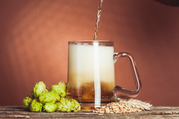 Vaso de cerveza con lúpulo y cebada en la mesa de madera