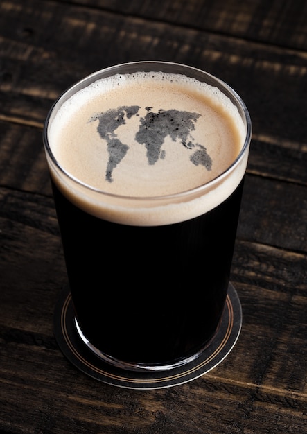 Vaso de cerveza negra con forma de mapa de tierra sobre fondo de madera