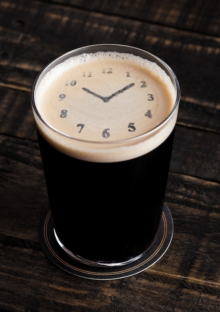 Vaso de cerveza negra con forma de reloj sobre fondo de madera