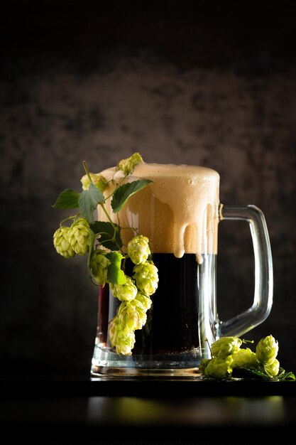 Vaso de cerveza oscura con lúpulo alrededor sobre un fondo oscuro