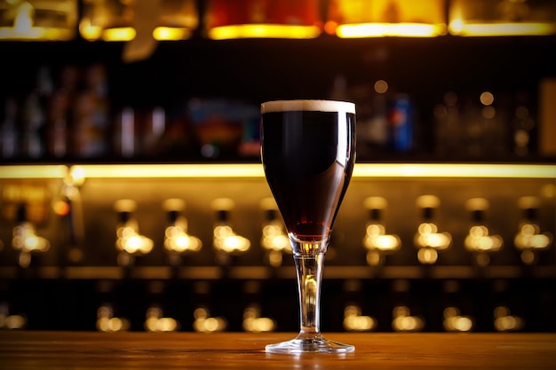 Un vaso de cerveza oscura en una pierna delgada en un bar.