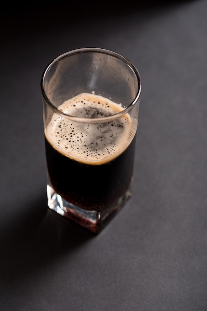 Foto vaso de cerveza oscura sobre un fondo de madera con textura oscura