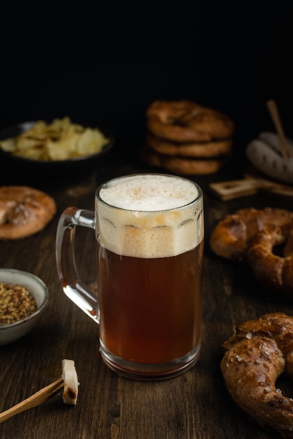 Vaso de cerveza con pretzels, salchichas y aperitivos en mesa de madera rústica