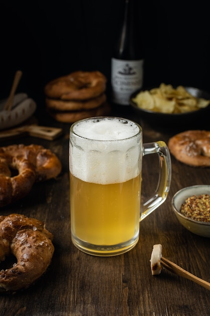 Vaso de cerveza con pretzels, salchichas y aperitivos en mesa de madera rústica