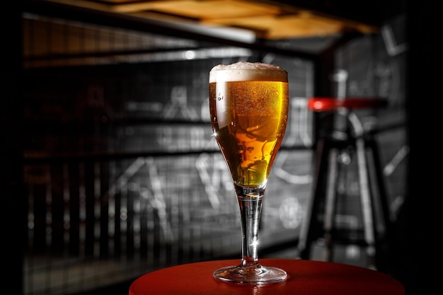 Un vaso de cerveza rubia en una pierna delgada en un bar.