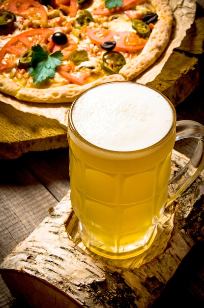 Vaso de cerveza en un soporte de abedul y la pizza en la mesa de madera