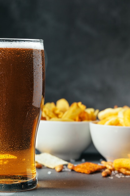 Vaso de cerveza con tazones de aperitivo en piedra oscura