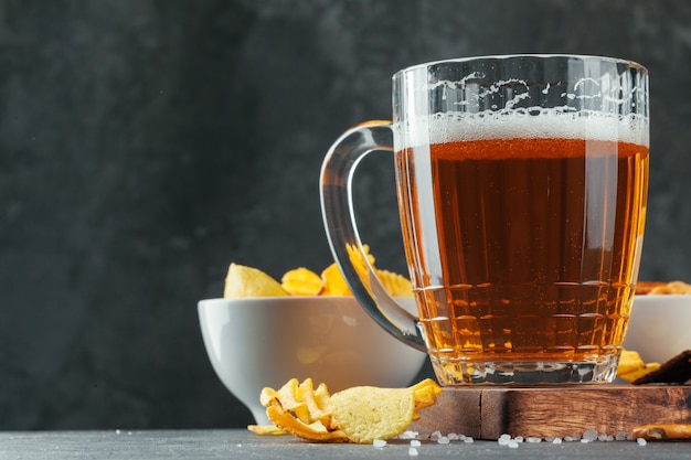 Vaso de cerveza con tazones de aperitivo en piedra oscura