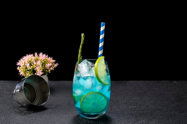 Vaso con cóctel azul decorado con limón y romero sobre fondo oscuro