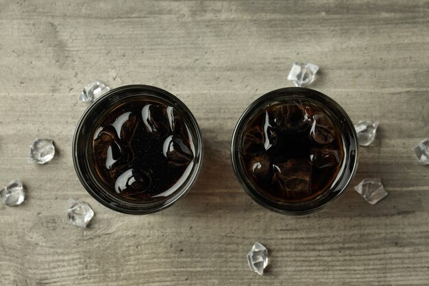 Vaso de cola y hielo en la mesa con textura gris.