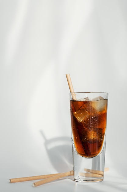 Vaso de cola con hielo y paja sobre una pared blanca