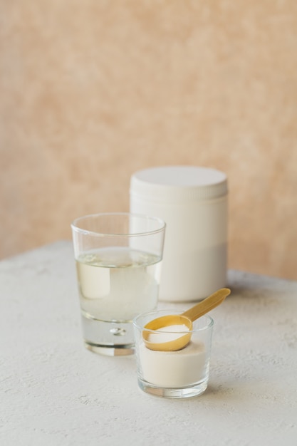 Vaso con colágeno disuelto en agua y proteína de colágeno en polvo sobre una mesa de color beige claro. Concepto de estilo de vida saludable.