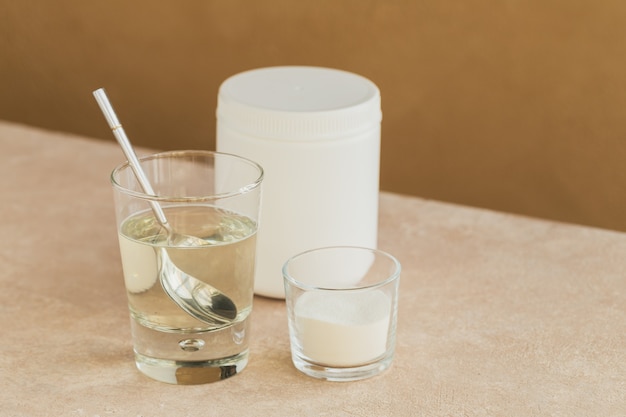 Vaso con colágeno disuelto en agua y proteína de colágeno en polvo sobre una mesa de color beige claro. Concepto de estilo de vida saludable.