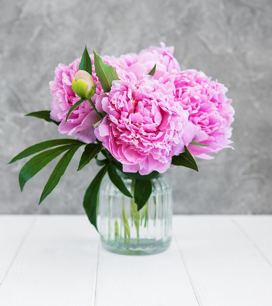 Vaso com flores de peônia rosa em uma mesa de madeira branca