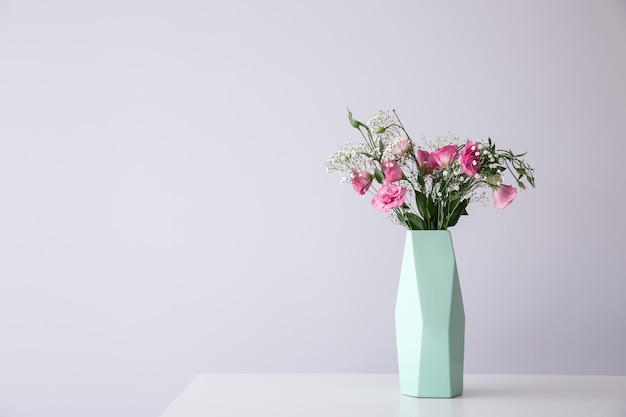 Vaso com lindas flores rosa na mesa contra um fundo claro