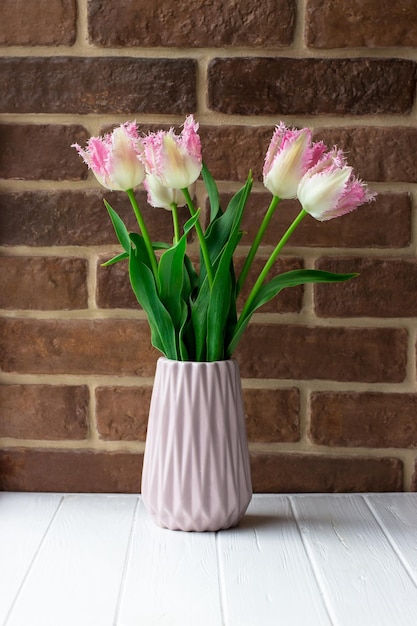 Vaso com tulipas em uma mesa branca Flores no fundo de uma parede de tijolos