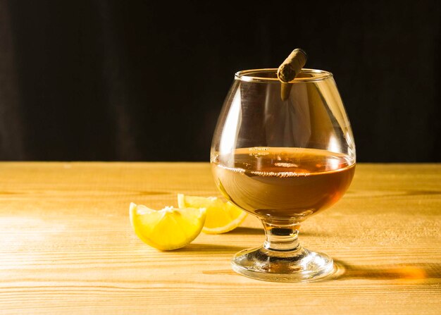 Un vaso de coñac en una mesa de madera una rebanada de limón y un cigarro en un vaso