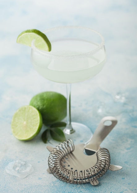 Foto vaso de cristal de cóctel margarita con limas frescas y filtro sobre un fondo azul claro