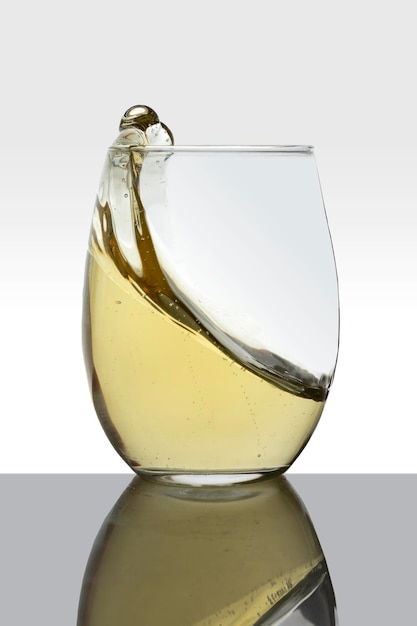 Vaso de cristal con vino blanco en movimiento haciendo olas y fondo blanco.