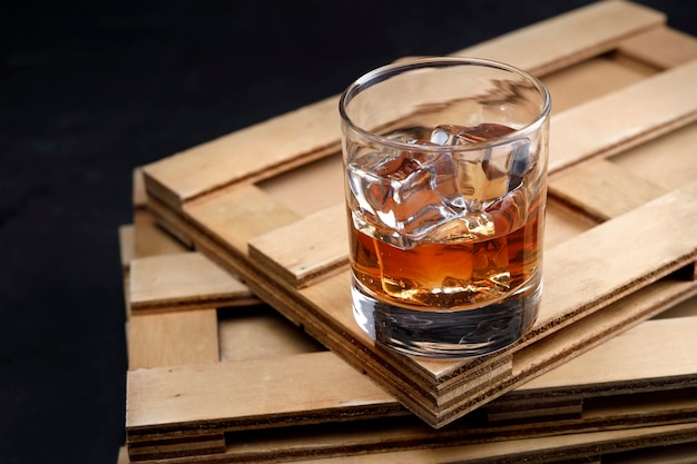 Vaso de cristal con whisky y hielo sobre mesa de madera