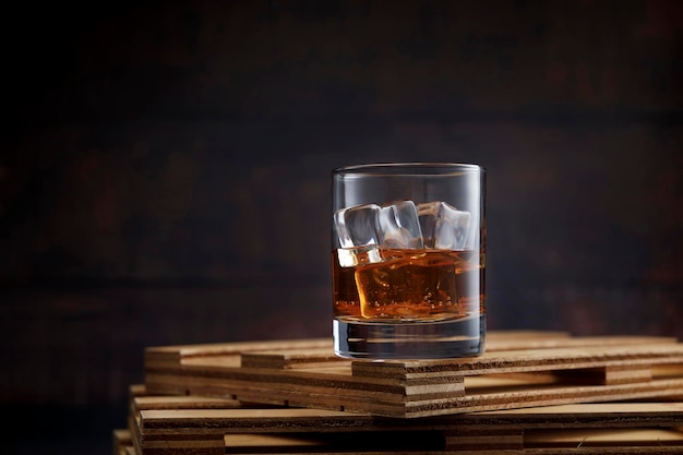 Vaso de cristal con whisky y hielo sobre mesa de madera